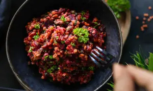 Ein herzhafter Linsen Rote Bete Salat, garniert mit Petersilie, wird mit einer Gabel aus einer dunklen Schüssel genommen.