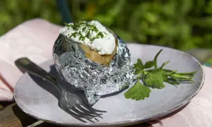 Folienkartoffeln vorkochen: Eine Kartoffel in Alufolie, belegt mit Quark und Kräutern, auf einem Teller mit Gabel und Petersilie.