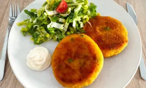 Zwei goldbraune, vegetarische Frikadellen mit einem frischen Salat und Mayonnaise auf einem Teller.
