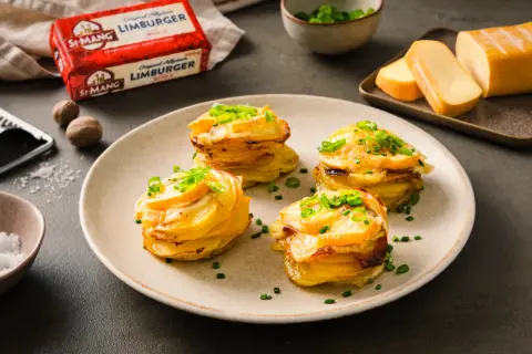 Gestapelte Kartoffeln mit geschmolzenem Käse und Schnittlauch. Daneben ein Block Limburger Käse, bereit für ein Romadur-Gericht.