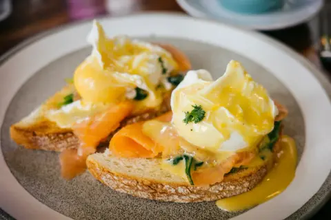 Zwei pochierte Eier auf Toast mit Lachs und Sauce Hollandaise. Ein köstliches pochierte Eier Rezept für ein perfektes Frühstück.