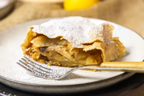 Ein Stück Apfelstrudel, bestäubt mit Puderzucker, wartet auf dem Teller. Dieses Apfelstrudel Rezept ist ein Genuss!