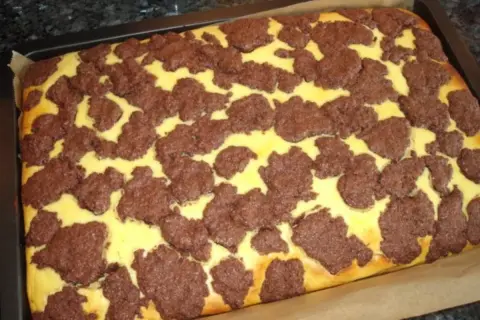 Ein frisch gebackener russischer Zupfkuchen im Blech, mit einem gelben Teig und dunklen Schokoladenstückchen darauf.