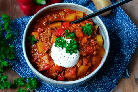 Herzhaftes Bauerntopf Rezept mit Hackfleisch, Kartoffeln und Paprika, garniert mit einem Klecks Sauerrahm und Petersilie.