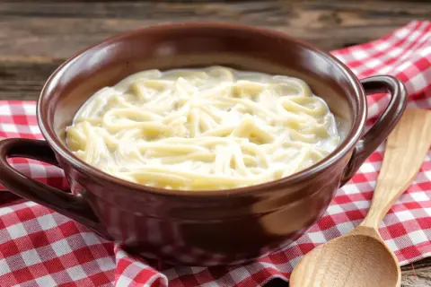 Eine Schüssel mit milch nudeln, serviert auf kariertem Stoff. Ein Holzlöffel liegt daneben.