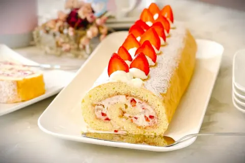 Eine köstliche Biskuitrolle mit Erdbeerfüllung, verziert mit frischen Erdbeeren und Sahnetupfern. Ein Klassiker, der an Omas Biskuitrolle Landfrauen erinnert.