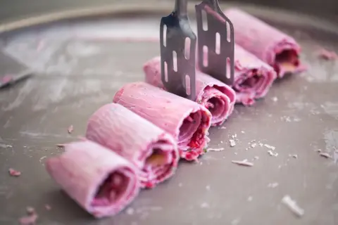 Eis selbst machen mit eismaschine: Rosa gerollte Eiscreme-Rollen werden mit zwei Spateln auf einer kalten Platte geformt.