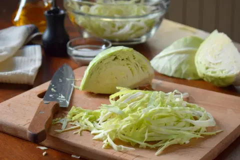 Frisch geschnittener Kohl liegt bereit für das Sauerkraut stampfen. Ein Messer und Gewürze sind auf dem Holzbrett arrangiert.