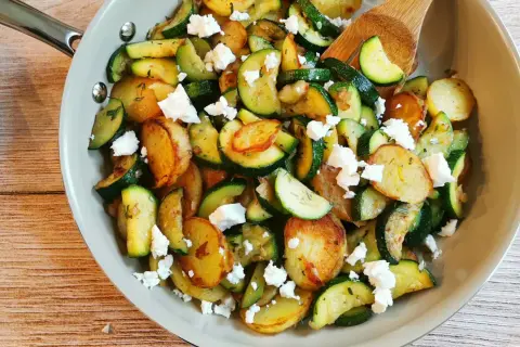 Herzhafte zucchini pfanne mit goldbraunen Kartoffelscheiben und zerbröckeltem Feta, garniert mit frischen Kräutern.