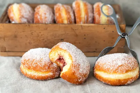 Frisch gebackene Berliner, mit Zucker bestreut, warten auf das perfekte Berliner Rezept. Eine Marmeladenfüllung ist sichtbar.