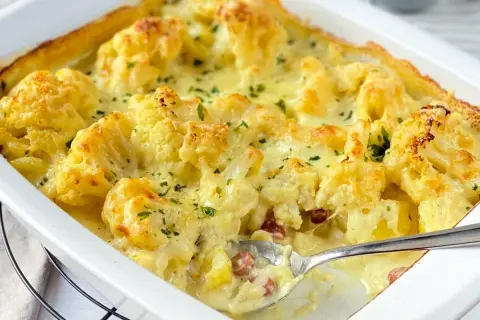 Herzhafte Blumenkohl-Rezepte: Cremiger Auflauf mit Käse überbacken, garniert mit Petersilie. Ein Löffel zeigt die leckere Füllung.