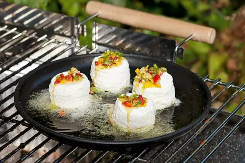 Vier runde Ziegenkäse auf einer Grillpfanne mit geschmolzenem Käse und Paprikastückchen. Perfekt für vegetarische Grillrezepte einfach.