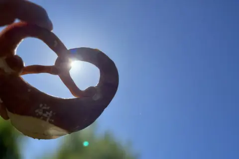 Ein Brezel wird gegen die Sonne gehalten. Woher kommen Brezeln? Aus dem Teig, der zu dieser Form geknetet wird.