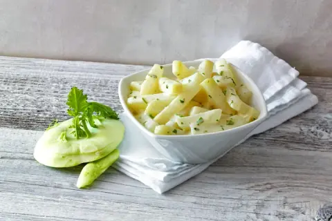 Kohlrabi kochen: zarte Kohlrabistücke in cremiger Sauce mit frischer Petersilie, daneben ein roher Kohlrabi.