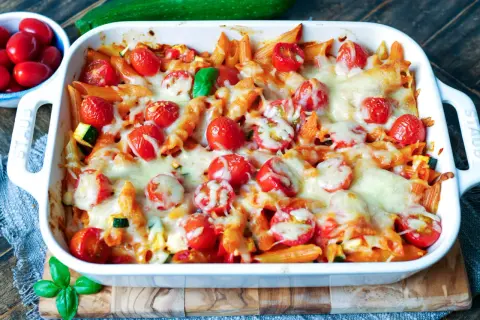 Ein köstlicher nudelauflauf vegetarisch mit Penne, Kirschtomaten und geschmolzenem Käse, garniert mit Basilikum.