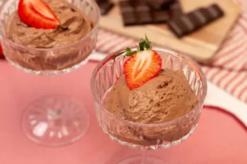 Zwei Gläser mit luftiger Schoko Mousse, garniert mit frischen Erdbeeren. Im Hintergrund liegen Schokoladenstücke.