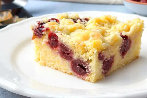 Ein saftiges Stück Kirsch-Streuselkuchen vom Blech auf einem weißen Teller, mit vielen Kirschen und knusprigen Streuseln.