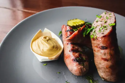 Zwei saftige, gegrillte Bratwürste mit Senf und Gurkenscheiben. Frische Bratwurst wie lange haltbar? Am besten sofort genießen!