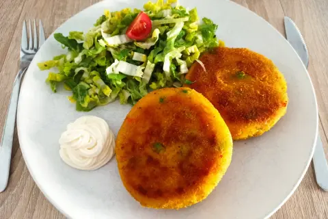 Zwei goldbraune, vegetarische Frikadellen mit einem frischen Salat und Mayonnaise auf einem Teller.