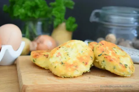 Goldbraune Macaire Kartoffeln, frisch zubereitet, liegen auf einem Holzbrett. Zutaten wie Eier und Petersilie sind im Hintergrund zu sehen.