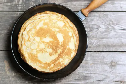 Ein Stapel goldbrauner, veganer Pfannkuchen liegt in einer Pfanne auf rustikalem Holz.