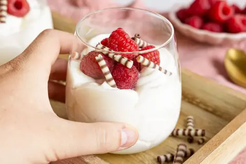 Ein Glas mit cremigem Quark-Dessert, garniert mit frischen Himbeeren und Schokoröllchen.