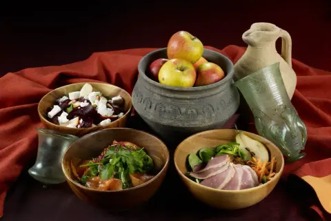 Essen wie im Mittelalter: Schalen mit Rote-Bete-Salat, Fleisch und Obst, dazu ein antiker Krug und Glas.