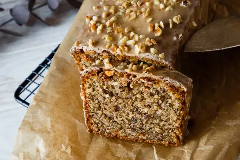 Ein saftiger Nusskuchen mit Zuckerguss und gehackten Nüssen, angeschnitten auf Backpapier.