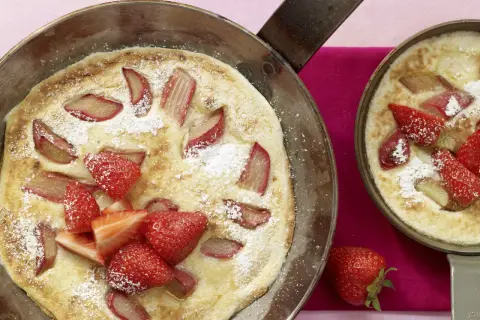 Zwei Pfannen mit frisch gebackenen Rhabarber-Pfannkuchen, garniert mit Erdbeeren und Puderzucker.