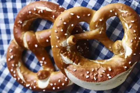 Zwei goldbraune Brezen mit grobem Salz liegen auf kariertem Stoff.