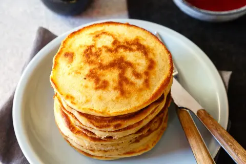 Stapel goldbrauner Dinkel Pancakes mit einem Muster auf dem obersten Pancake, serviert auf einem hellblauen Teller mit Messer und Gabel.