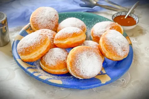 Ein Teller voller frisch gebackener Krapfen, bestäubt mit Puderzucker. Dieses Krapfen Rezept ist ein Genuss!