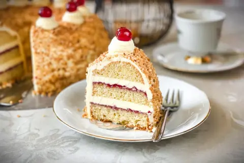 Ein Stück Frankfurter Kranz mit Buttercreme, Marmelade und gehackten Nüssen, garniert mit einer Kirsche.