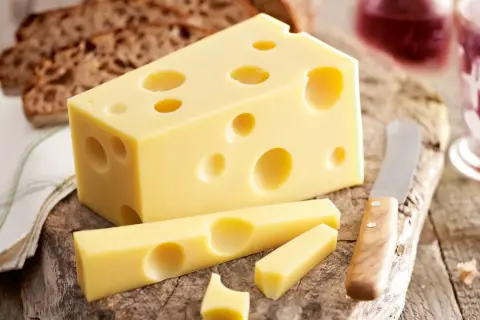 Ein Stück Emmentaler mit seinen charakteristischen Löchern, daneben Brot und ein Glas Rotwein. Die Herkunft des Käses ist unverkennbar.