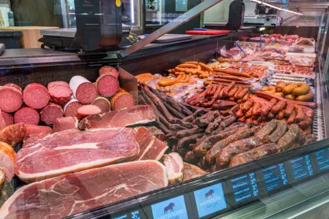 Reichhaltige Auswahl an bayerischer Wurst und Schinken, von Salami bis hin zu deftigen Rohwürsten, appetitlich präsentiert in einer Kühltheke.