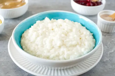 Cremiger Milchreis im blauen Schüsselchen, perfekt für ein einfaches Milchreis Rezept. Dazu Apfelmus und Kirschen.
