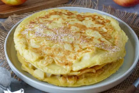 Ein Stapel goldbrauner Apfelpfannkuchen, bestäubt mit Puderzucker. Ein köstliches Apfelpfannkuchen Rezept zum Genießen.