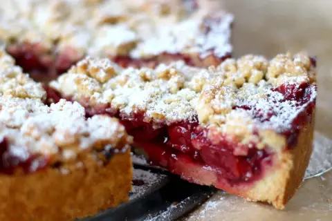 Ein Stück saftiger, schneller Kirsch-Streuselkuchen, bestäubt mit Puderzucker. Die roten Kirschen leuchten unter den knusprigen Streuseln hervor.