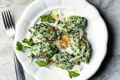 Malfatti Rezept: Grüne Klößchen aus Spinat und Ricotta, garniert mit Parmesan und Petersilie, auf einem weißen Teller.