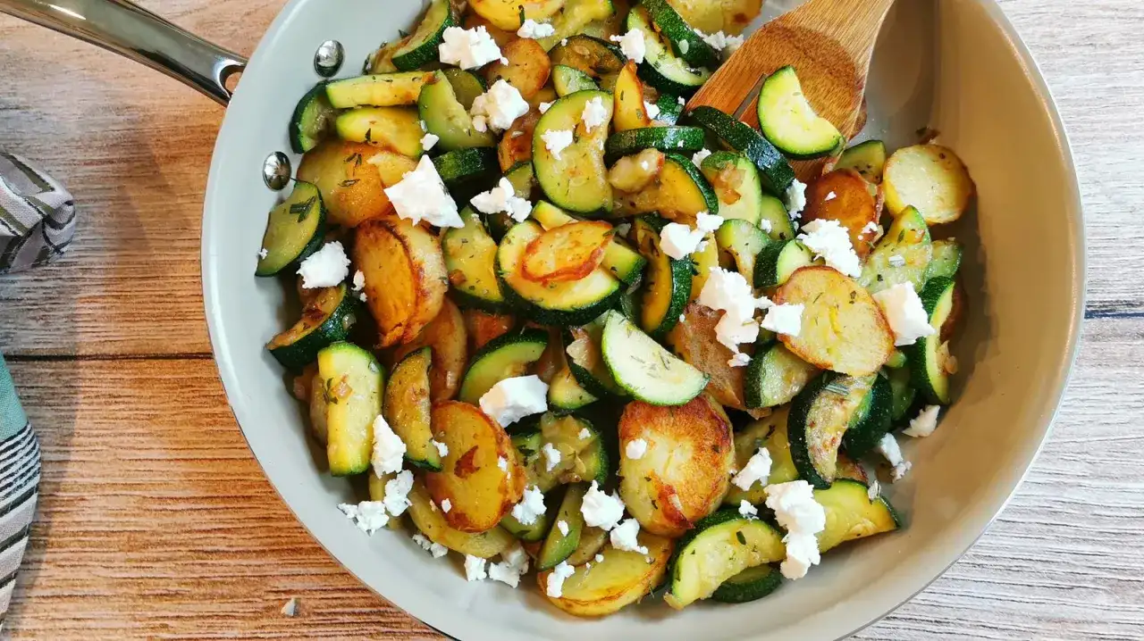 Herzhafte zucchini pfanne mit goldbraunen Kartoffelscheiben und zerbröckeltem Feta, garniert mit frischen Kräutern.