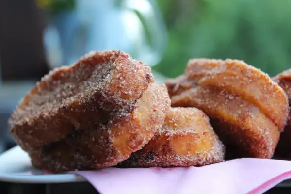 Süße Zwetschgen Bavesen, goldbraun frittiert und in Zimt-Zucker gewälzt, liegen auf einem rosa Tuch.
