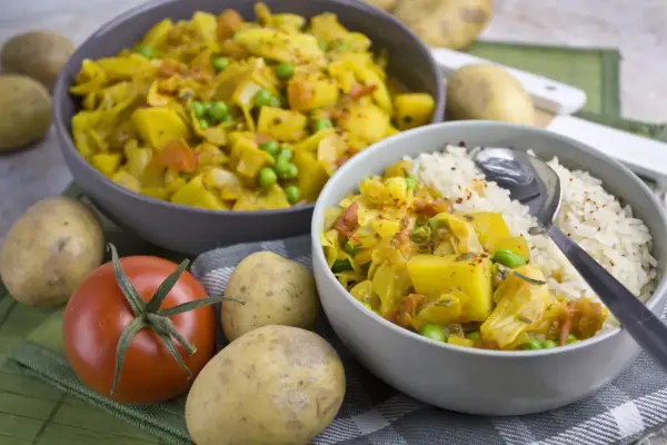 Herzhaftes Gericht mit Kartoffeln, Erbsen und Kohl, erinnert an bremer scheerkohl. Daneben Reis und frische Zutaten.