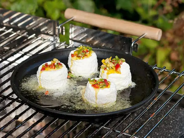 Vier runde Ziegenkäse auf einer Grillpfanne mit geschmolzenem Käse und Paprikastückchen. Perfekt für vegetarische Grillrezepte einfach.